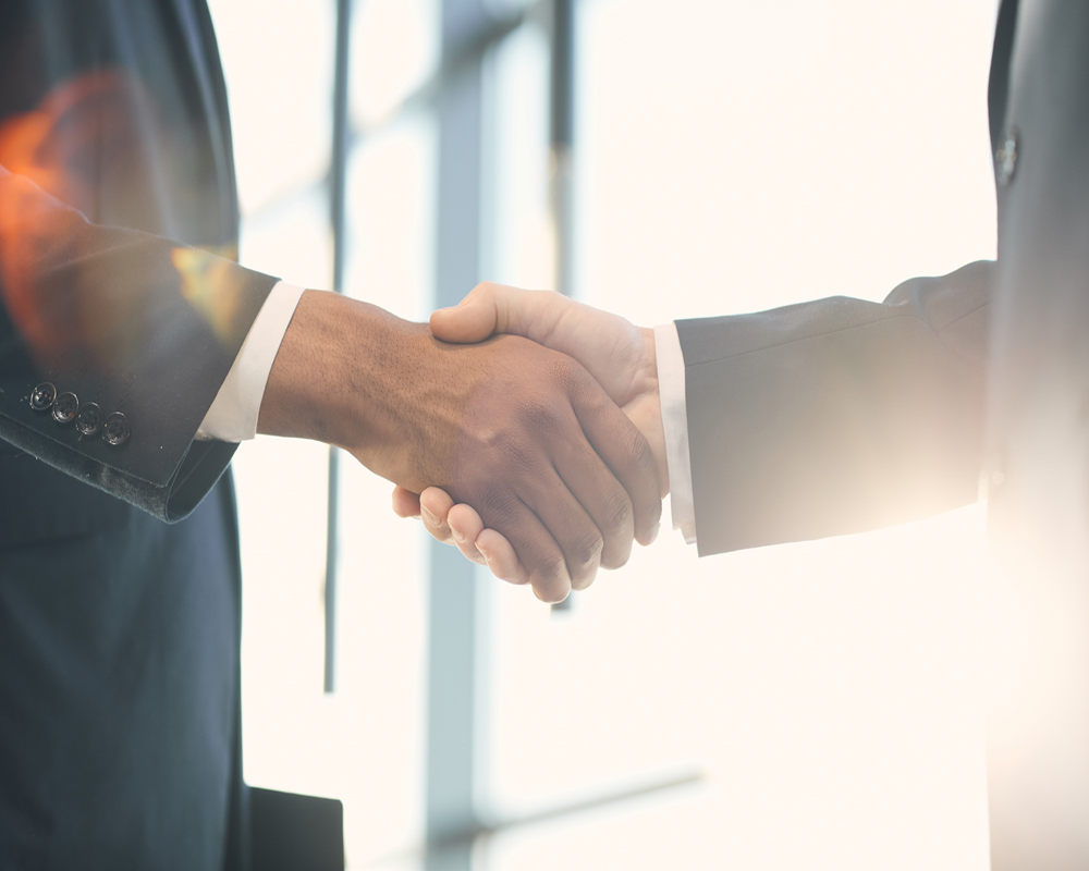 Close-up of unrecognizable multi-ethnic business partners in suits handshaking in light, gesture symbolizing trust and respect